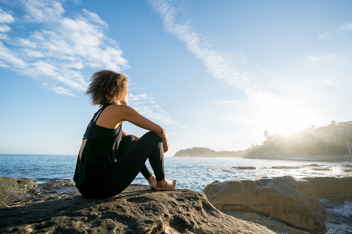 Ab nach draußen gegen Stress: Frau entspannt auf Felsen am Meer