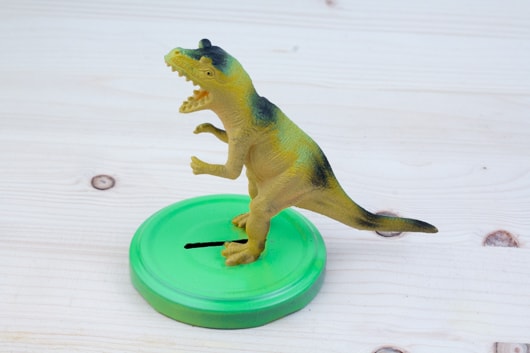 Een dinosaurusfiguur is op het deksel gelijmd.