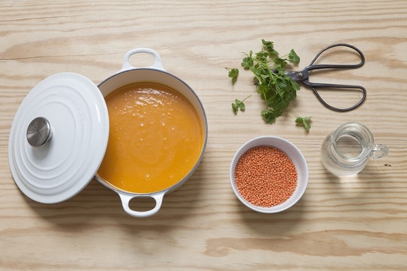 Une soupe au potiron dans une soupière avec une carafe d'eau, des lentilles et de la coriandre fraîche