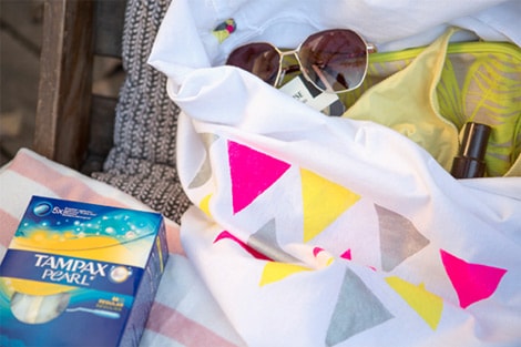 Le sac créé avec une paire de lunettes de soleil et des accessoires posés sur un transat, avec boite de tampax.