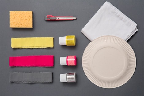 Une éponge, un cutter, du tissu, des colorant, des serviettes en papier et une assiette en carton.