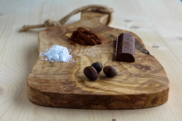 Planche en bois sur laquelle il y a du chocolat dur, des noisettes, du sucre glace et du chocolat en poudre