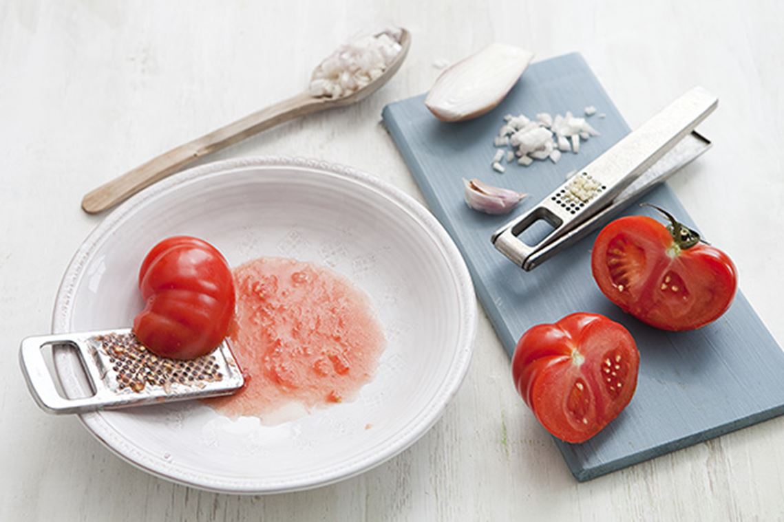 Halve tomaten gerapt op een bord, kleine stukjes sjalot in een lepel, geraspte stukjes knoflook