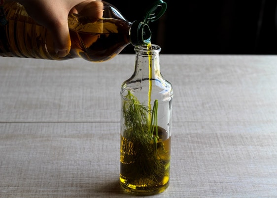 Een persoon giet olijfolie in een fles met aromatische kruiden