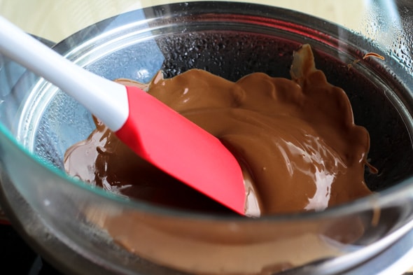 Een rode spatel roert gesmolten chocolade in een kom.