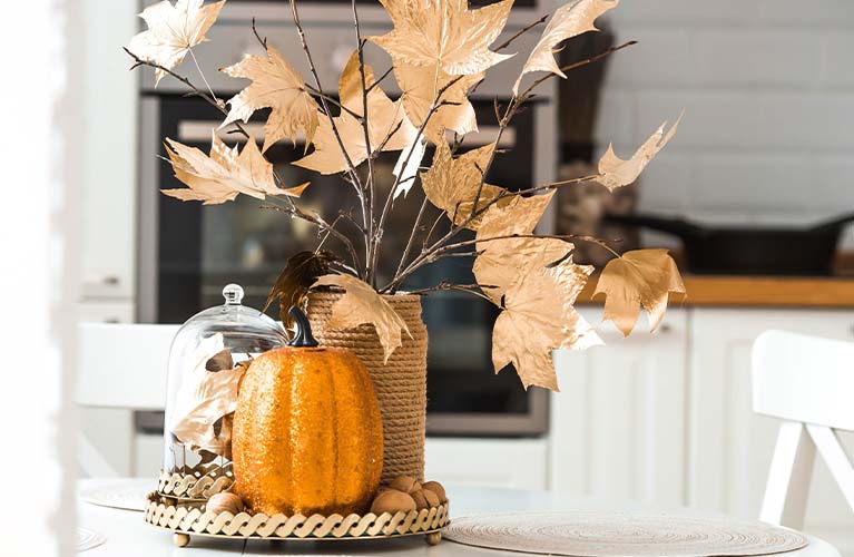Herbst-Deko-Idee: Tasse, Kerzenhalter, Kuscheldecke und Lichterkette auf einem Tisch. 
