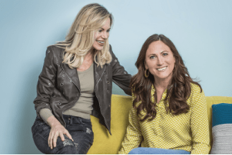 Nina Ruge und Sennerin Martina Fischer sitzen auf einem gelben Sofa und lächeln. Auf der blauen Wand hinter ihnen sieht man das Victoria-Logo.