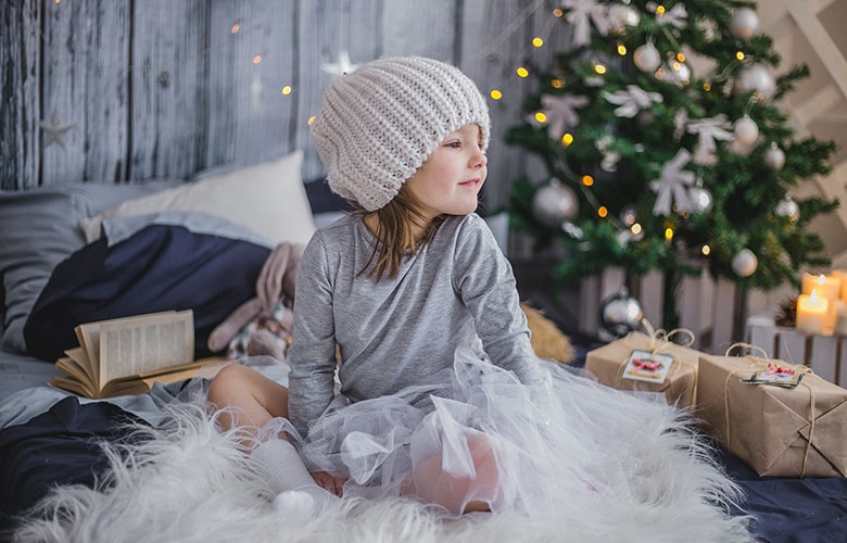 Κορίτσι φοράει σκούφο και τούλι, κάθεται στο κρεβάτι με δώρα και χριστουγεννιάτικο δέντρο
